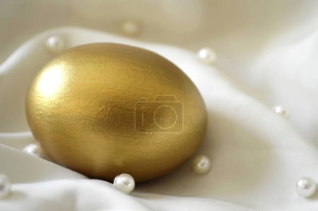 Photo for Golden easter egg on white textile with pearls - Royalty Free Image