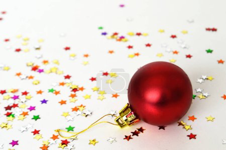 Foto de Bola de Navidad roja y estrellas confeti sobre fondo blanco. - Imagen libre de derechos