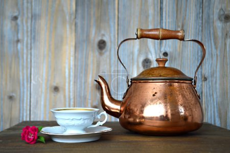 Foto de Tetera de cobre y elegante taza de té blanco con flor en la mesa - Imagen libre de derechos