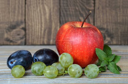 Foto de Manzana roja fresca, ciruelas y uvas sobre una mesa de madera - Imagen libre de derechos