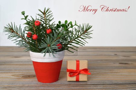 Plantilla de tarjeta de Feliz Navidad. Ramas de pino con beries rojos en maceta y pequeño regalo envuelto 
