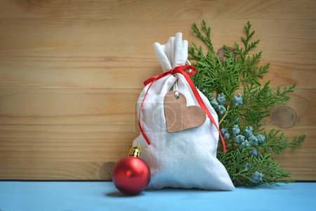 Téléchargez les photos : Décorations de Noël sur fond bois, petit sac rustique, boule rouge brillant et brindilles vertes - en image libre de droit