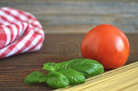 Foto de Antecedentes de comida italiana. tomate fresco, hojas de albahaca, espaguetis crudos, granos de pimienta y paño a cuadros - Imagen libre de derechos