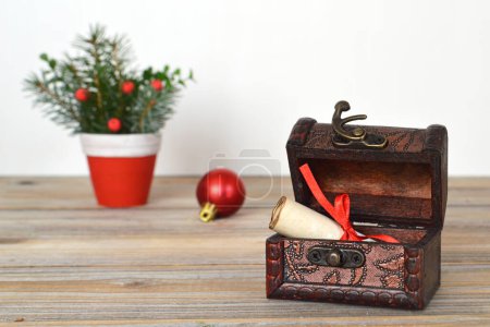 Photo for Pot with spruce twigs, red shiny christmas ball and old vintage chest with paper scroll wrapped up with red ribbon. - Royalty Free Image