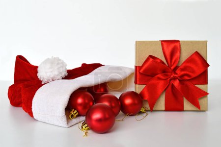 Foto de Decoraciones de Navidad, sombrero de santa rojo con adornos brillantes y caja de regalo envuelta con cinta roja aislada sobre un fondo blanco - Imagen libre de derechos