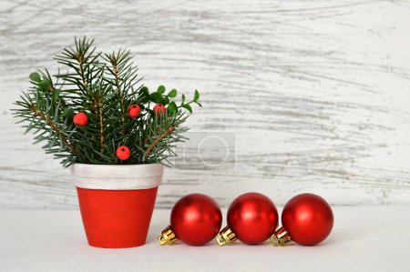 Téléchargez les photos : Décorations de Noël sur la table, pot avec des brindilles de pin et des baies rouges, boules rouges brillantes - en image libre de droit