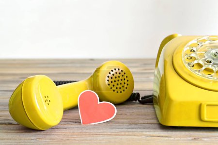 Photo for Vintage yellow telephone and heart shaped tag on wooden background - Royalty Free Image
