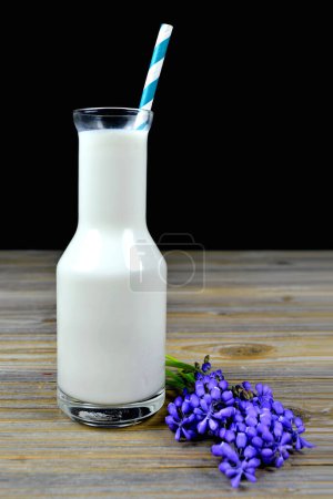 Téléchargez les photos : Bouteille de lait avec paille rayée et fleurs violettes sur table en bois - en image libre de droit