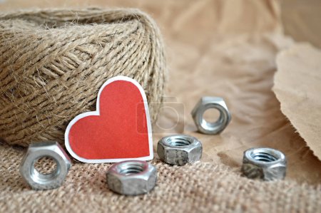 burlap rope, heart shape red sticker and hex nuts on burlap cloth background