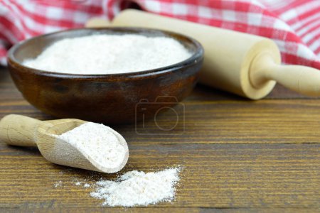Téléchargez les photos : Farine de blé entier dans un bol en bois, cuillère en bois et rouleau à pâtisserie sur la table - en image libre de droit