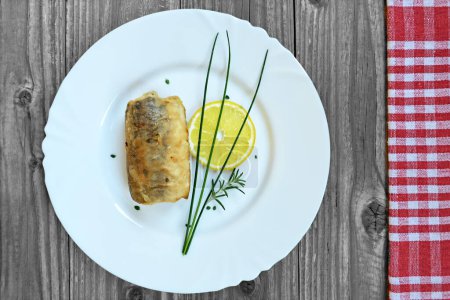 Foto de Filete de pescado frito con rodaja de limón y hierbas en plato blanco - Imagen libre de derechos
