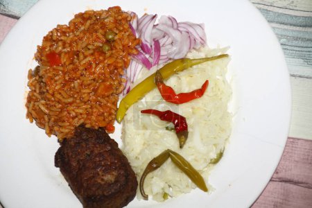 close-up of a Balkan dish with pljeskavica, djuvec rice, onions, coleslaw, pepperoni served on a white plate,