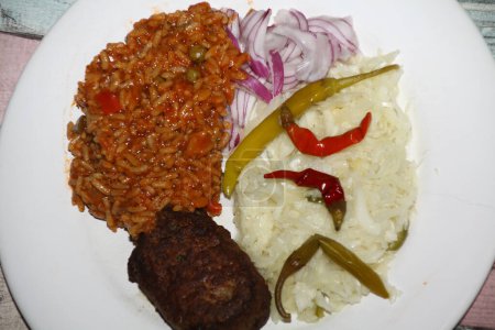 primer plano de un plato balcánico con pljeskavica, arroz djuvec, cebolla, ensalada de col, pepperoni servido en un plato blanco,