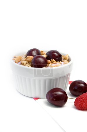 Téléchargez les photos : Petit déjeuner sain avec céréales, yaourt, cerises et framboises dans un bol blanc vertical - en image libre de droit