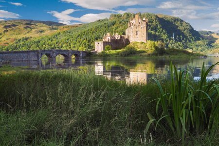 Téléchargez les photos : Château d'Eilean Donan à l'heure dorée du petit matin. Château écossais médiéval reflétant dans l'eau par une belle journée d'été. Château dans les hautes terres écossaises. Patrimoine culturel de l'Écosse - en image libre de droit