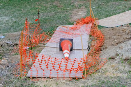 Orange construction fence and traffic cone laying on brown cardboard dirt embankment cover at roadside. Infrastructure repair construction site maintenance work at sidewalk curb city street view photo