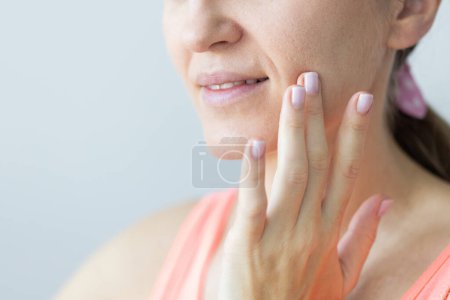 Young smiling woman gently touching her face with fingers. Nasolabial wrinkles, problem dry skin with big pores. Skin care concept.