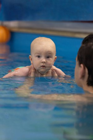 Porträt des neugierigen Babys in einem Schwimmbad. Schwimmen mit einem Trainer