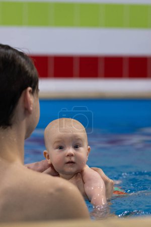 Porträt des neugierigen Babys mit Schwimmtrainer in einem Schwimmbad. Schwimmunterricht für Neugeborene