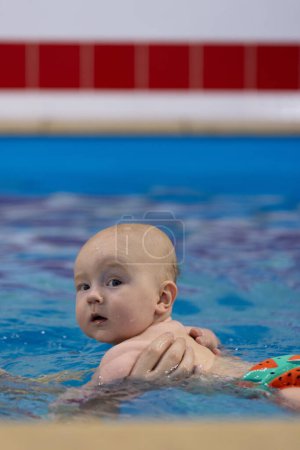 Porträt des neugierigen Babys in einem Schwimmbad. Schwimmen mit einem Neugeborenen. 
