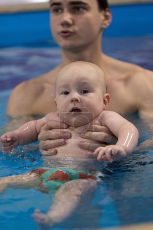 Porträt des neugierigen Babys mit Schwimmtrainer in einem Schwimmbad. Schwimmunterricht für Neugeborene