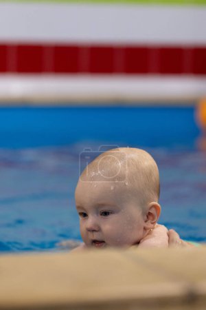 Porträt des Babys in einem Schwimmbad. Nahaufnahme. Baby hat Wassertropfen im Gesicht, nachdem es unter Wasser getaucht ist. Selektiver Fokus