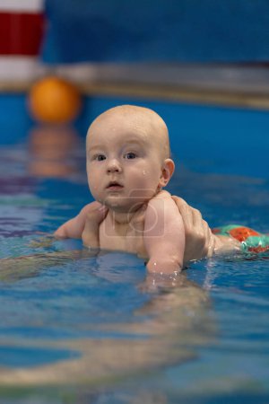 Porträt des neugierigen Babys in einem Schwimmbad. Schwimmen mit dem Trainer
