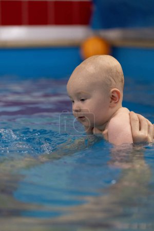 Lächelndes Baby in einem Schwimmbad. Schwimmen mit Neugeborenen. Nahaufnahme.