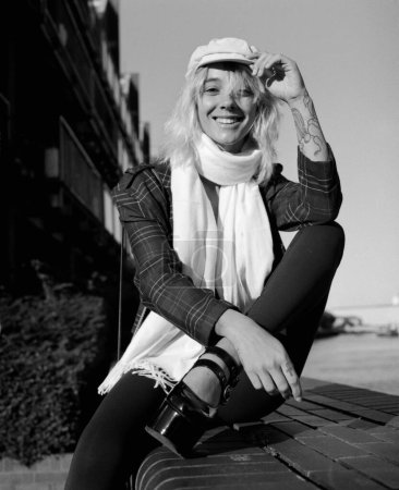 Téléchargez les photos : Smiling alternative female model is looking at camera sitting on stairs outside. Image made with medium format analog film camera. Monochrome. - en image libre de droit