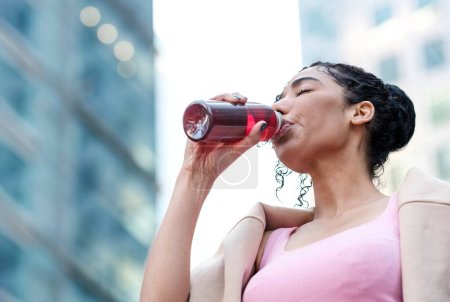 Téléchargez les photos : Portrait d'une jeune femme de fitness buvant de l'énergie dans une bouteille. Elle a les yeux fermés et porte un soutien-gorge de sport rose et un pull sur les épaules. Concept de fitness et d'hydratation. Mode de vie sain. - en image libre de droit