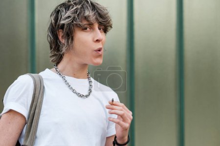 Foto de Persona no binaria que fuma al aire libre. Hay un fondo verde detrás. Concepto de libertad de elección. - Imagen libre de derechos
