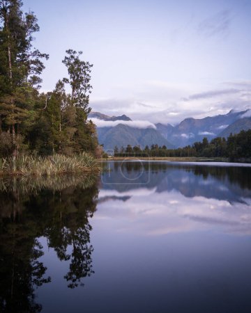 Beau lac entouré de forêts exotiques et de montagnes en arrière-plan pendant le coucher du soleil, Nouvelle-Zélande.
