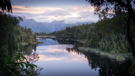 Beautiful colorful sunset over a lake surrounded by forest and mountains in backdrop in New Zealand.