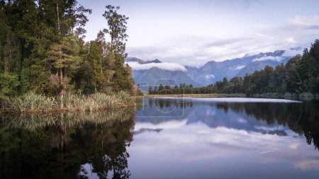 Beau lac entouré de forêts exotiques et de montagnes en arrière-plan pendant le coucher du soleil, Nouvelle-Zélande.