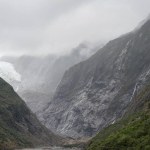 Wide shot of massive glacier flowing into a valley through steep rock walls shot in New Zealand.
