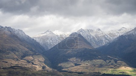 Photo for View on snowy mountains rising from green pastures during overcast cloudy day, New Zealand. - Royalty Free Image