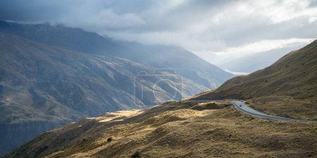 Cars passing curvy road leading through mountains pass in alpine environment, New Zealand.