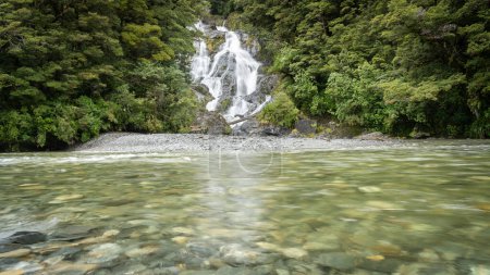 Beautiful forest waterfall with river flowing in front of it, New Zealand.