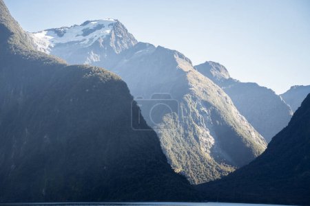 Paisaje de fiordos con frondoso bosque y pico alto con glaciares que se elevan sobre el mar, Nueva Zelanda.