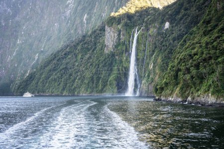 Photo for Tourist sightseeing boat approaching big waterfall in fjord falling into sea, Fiordland, New Zealand. - Royalty Free Image