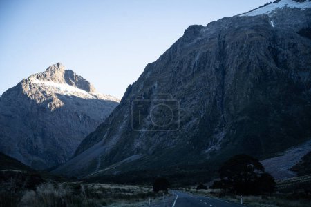 Carretera vacía que conduce a través del valle con empinadas paredes rocosas en Fiordland, Nueva Zelanda.