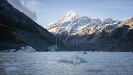 Glacial lake with big floating pieces of ice and dominant snowy mountain in backdrop, New Zealand.