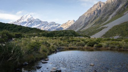 Small alpine pond surrounded by mountains with snowy peak in background, Mt Cook, New Zealand.