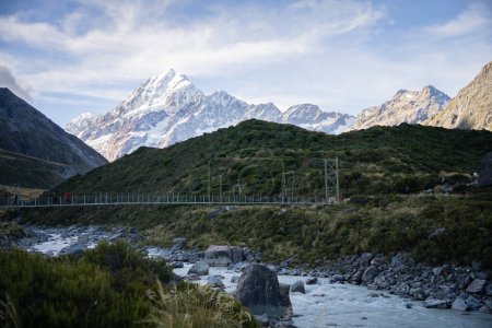 Tourists crossing swing bridge above glacial river in alpine environment, Mt Cook, New Zealand.