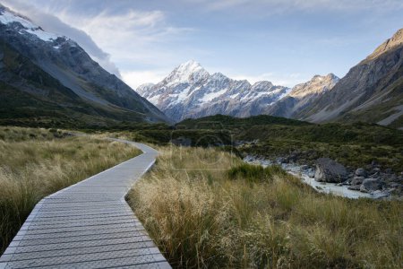 Wooden boardwalk leading through beautiful alpine valley with snowy mountain in backdrop,New Zealand.