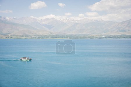 Sightseeing boat with tourists sailing on beautiful blueish lake with mountains in backdrop, Turkey.