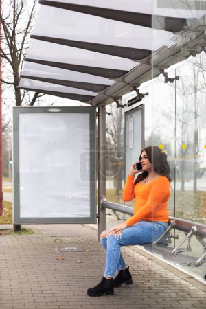 Vertikale Aufnahme einer Transfrau, die in einer Bushaltestelle mit dem Handy spricht. Hochwertiges Foto