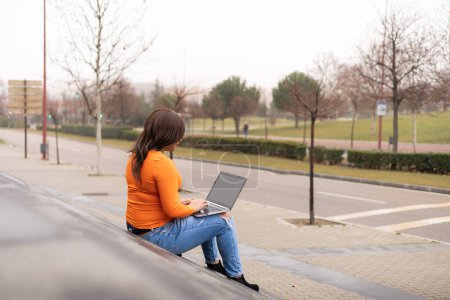 Photo for Rear view of trans woman using laptop in campus stairs. General view of campus. High quality photo - Royalty Free Image