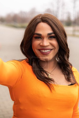 Selfie of trans woman in orange clothes. Latin ethnicity. City outdoors. High quality photo