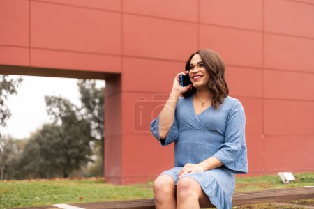 Trans woman sat in modern outdoors talking in cellphone. High quality photo